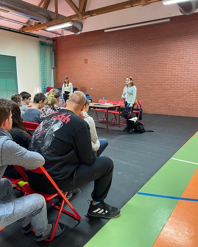 Instructor with a dog in harness talking to a room of students